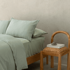 Close-up of the sage green quilt cover and pillowcases styled beside a natural timber chair, highlighting the soft washed texture and relaxed finish.