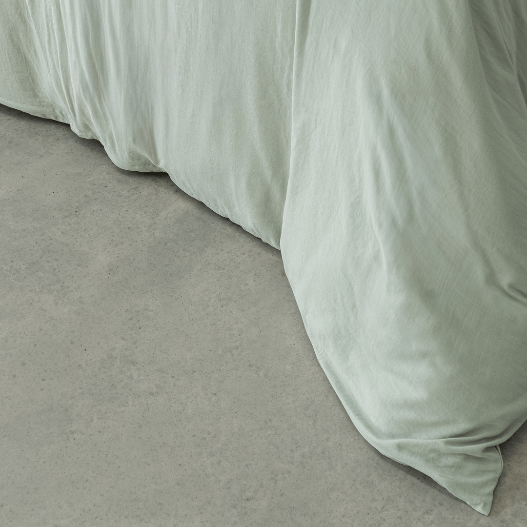 Detailed view of the sage green quilt cover fabric draping naturally over the bed edge, showcasing its lightweight feel and casual elegance.