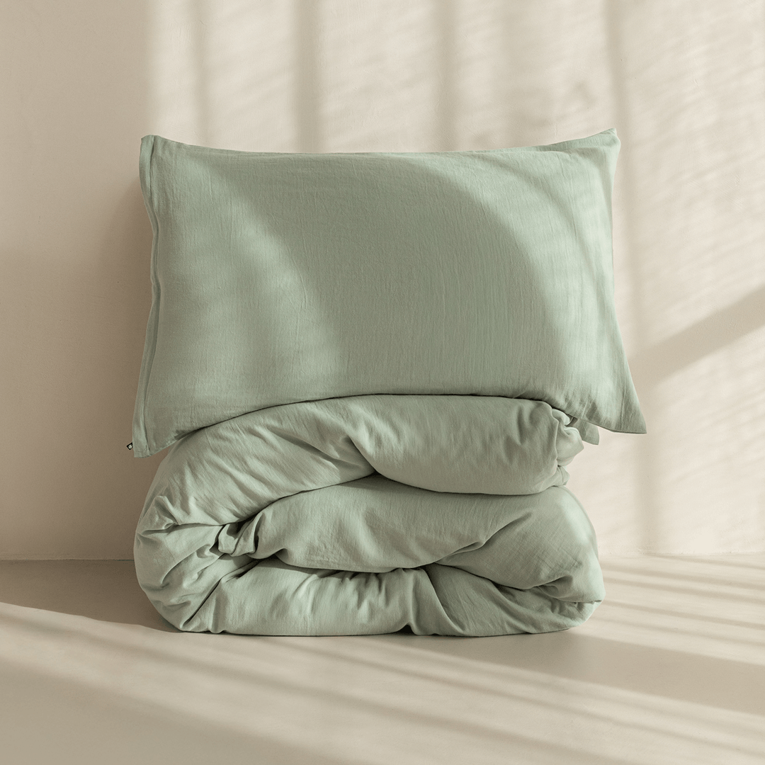 Folded sage green quilt cover and pillowcase set displayed in natural light, showcasing the soft washed fabric and premium craftsmanship.