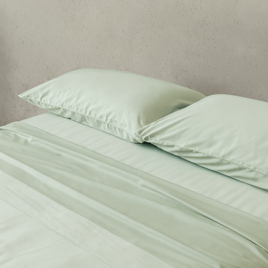 Close-up of matching sage green pillowcases and fitted sheet, highlighting the silky-soft fabric, smooth texture, and coordinated bedding design.