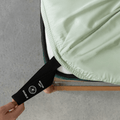 Close-up of the fitted sheet secured around the mattress corner, highlighting the elastic edge and orientation tag for quick installation.
