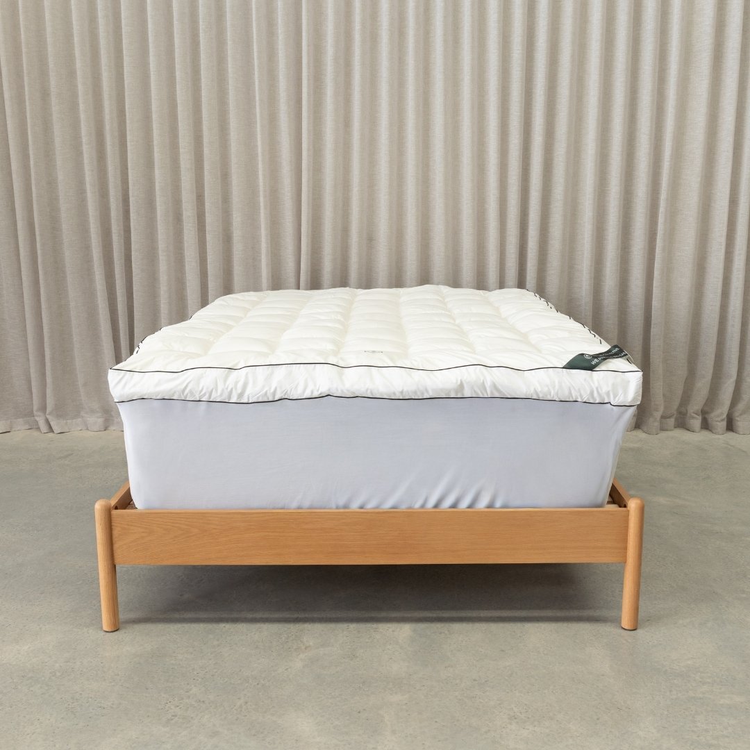 Mattress topper on a bed and wooden bed frame against a beige curtain background.