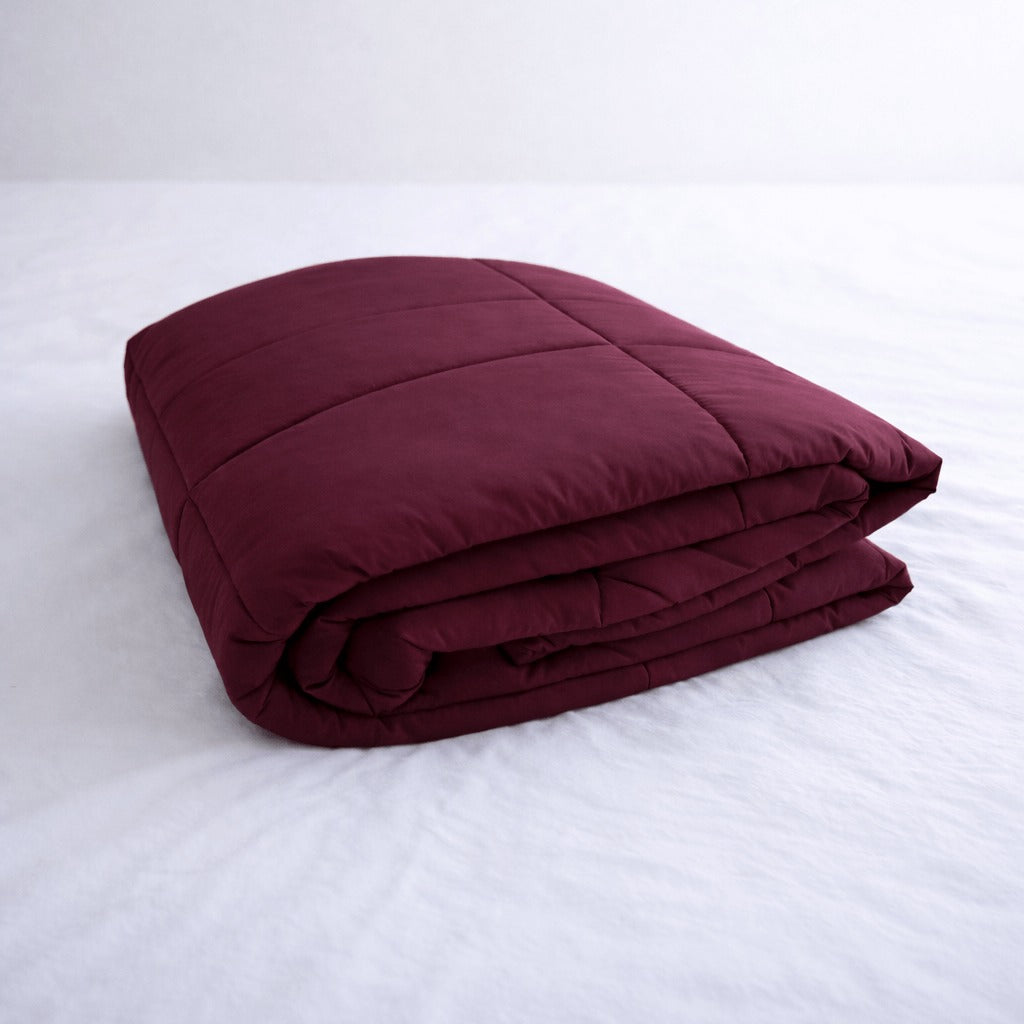 Folded burgundy cooling blanket on a white bed.