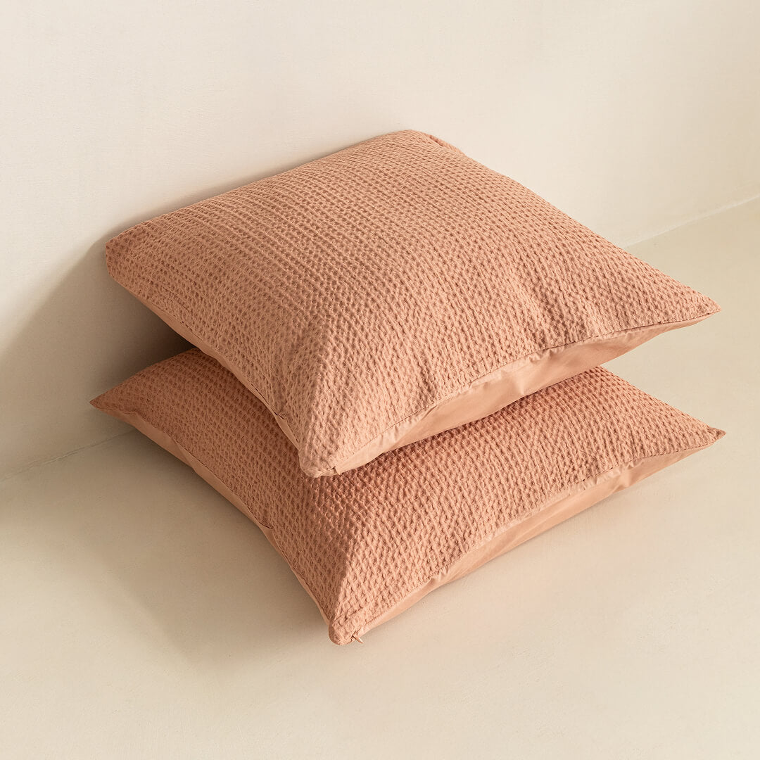 Two textured clay, European pillows stacked on a light beige surface.