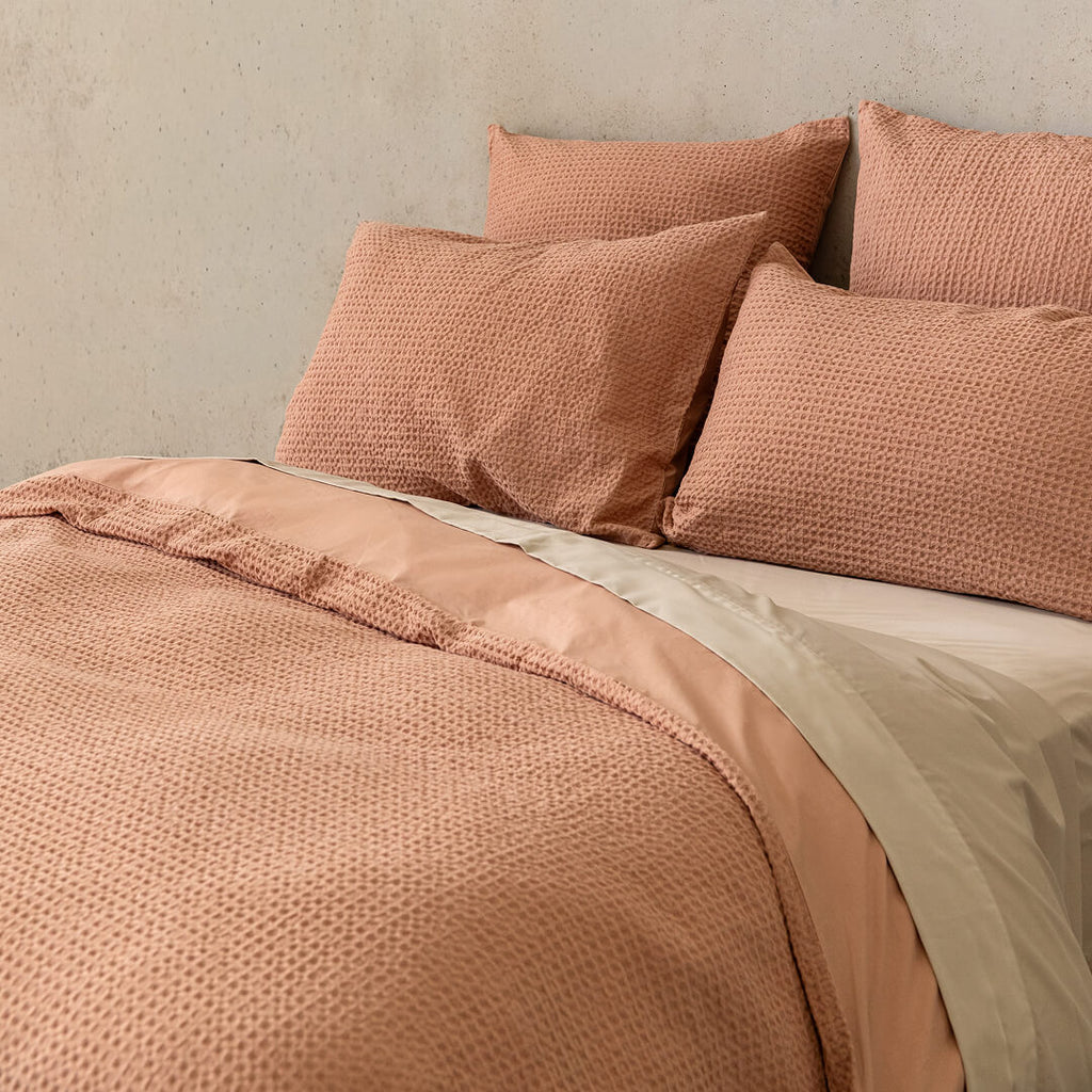 Close-up of a textured pink bedspread and pillows on a neutral background.