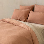 Close-up of a textured pink bedspread and pillows on a neutral background.