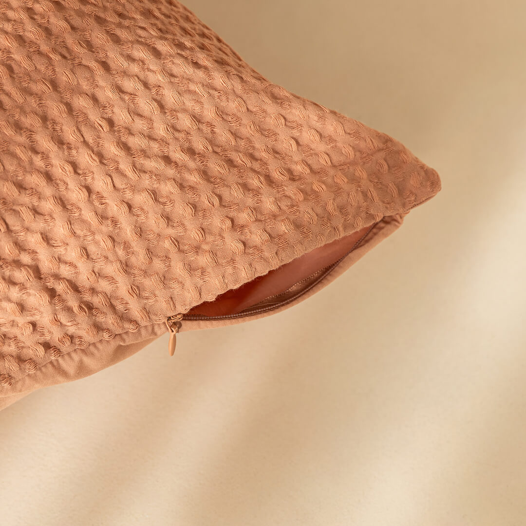 Textured waffle, clay coloured pillow on a beige background. Showcasing invisible zip feature.