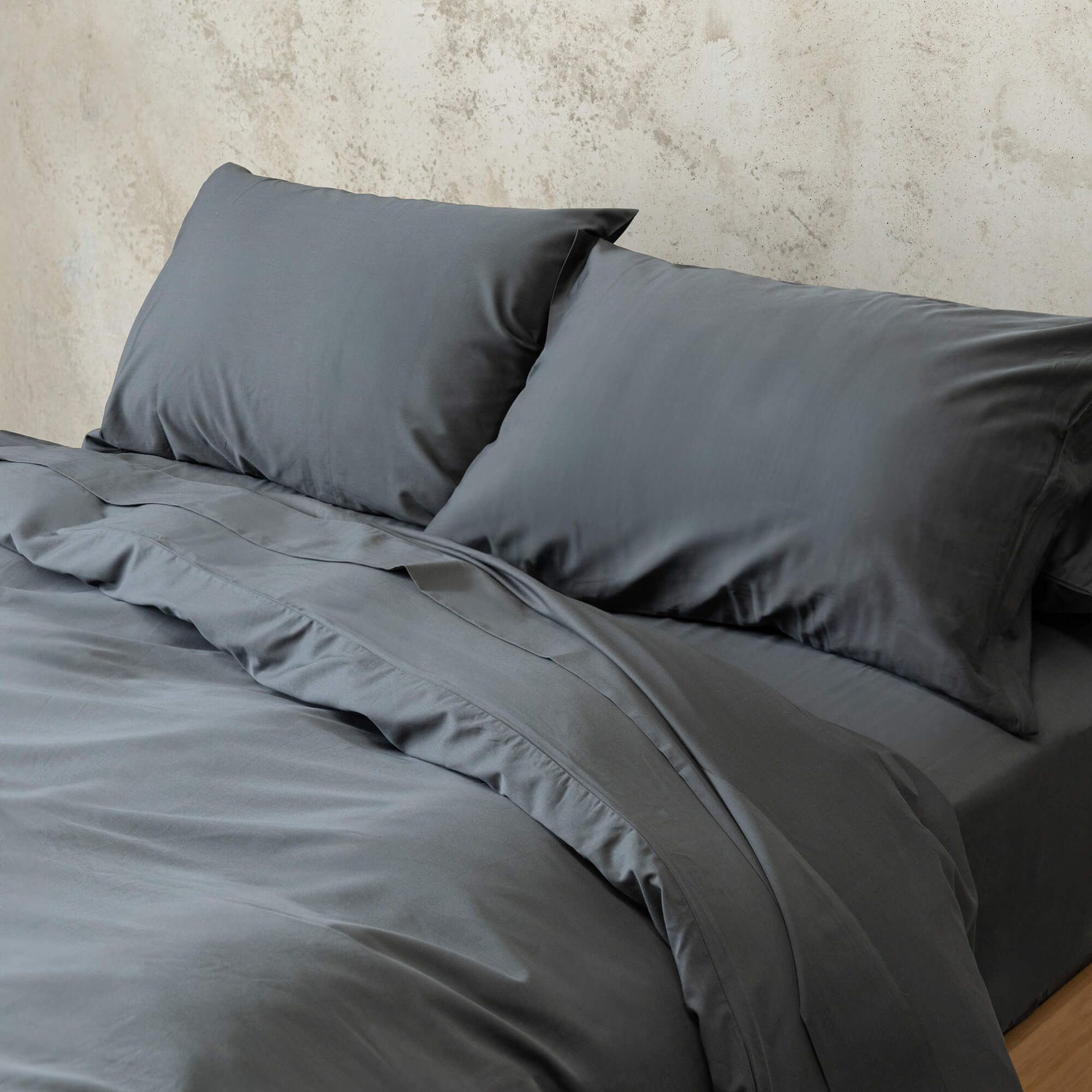 Dark grey bedding set on a bed against a plain wall.