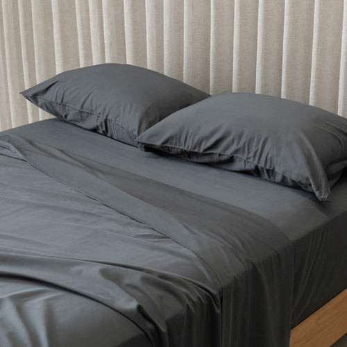 Grey bedspread on a bed with pillows against a beige curtain background