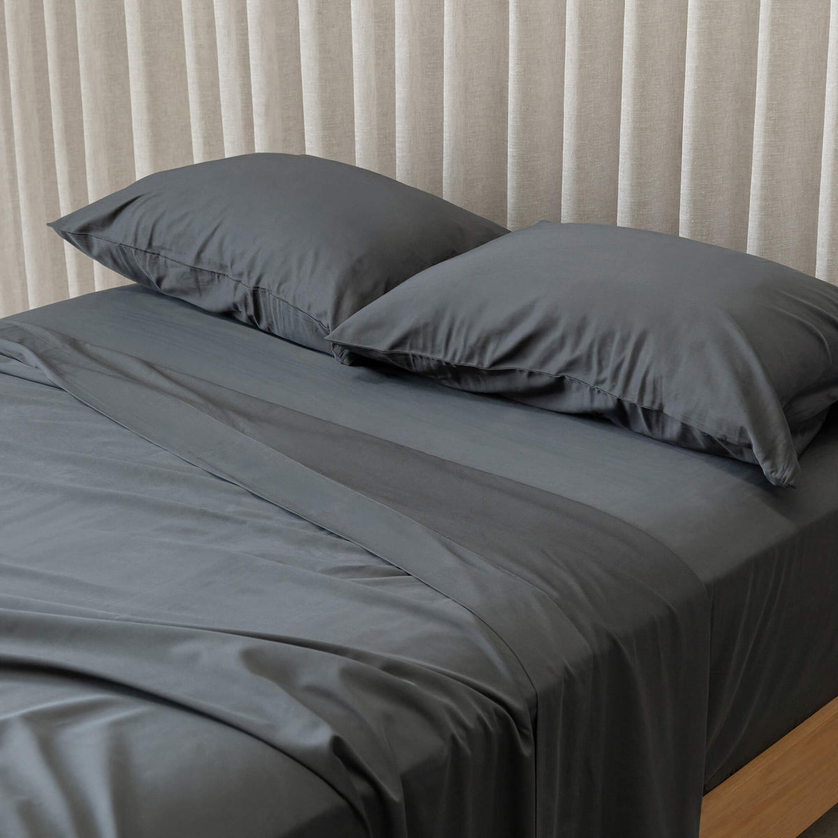 Grey bedding set with two pillows on a bed against a neutral curtain background