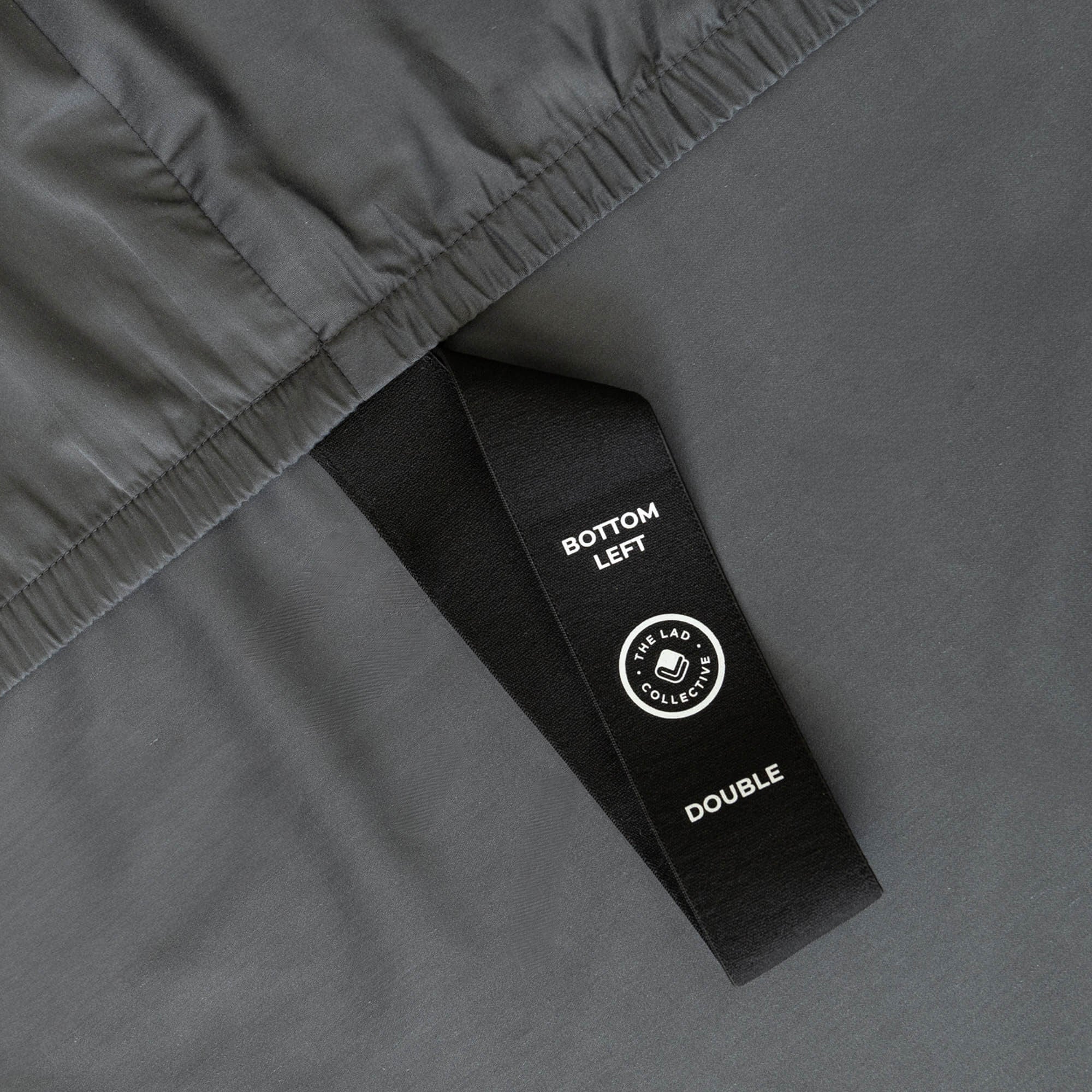 Close-up of a grey fabric with a black labelled loop strap on a matching grey background.