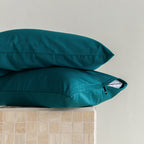 Two teal pillows stacked on a beige surface with a neutral background.