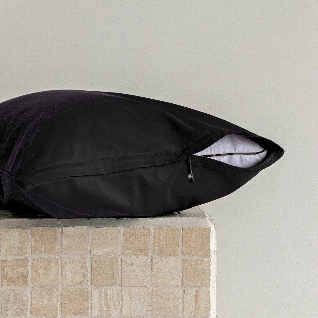 Black pillow on a textured surface with a neutral background, showcasing the half open invisible zip on the pillowcase.