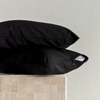 Two black pillows stacked on a light gray surface with a neutral-colored wall in the background.