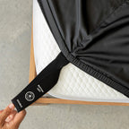 Black bed sheets with corner strap on a bed with a neutral background