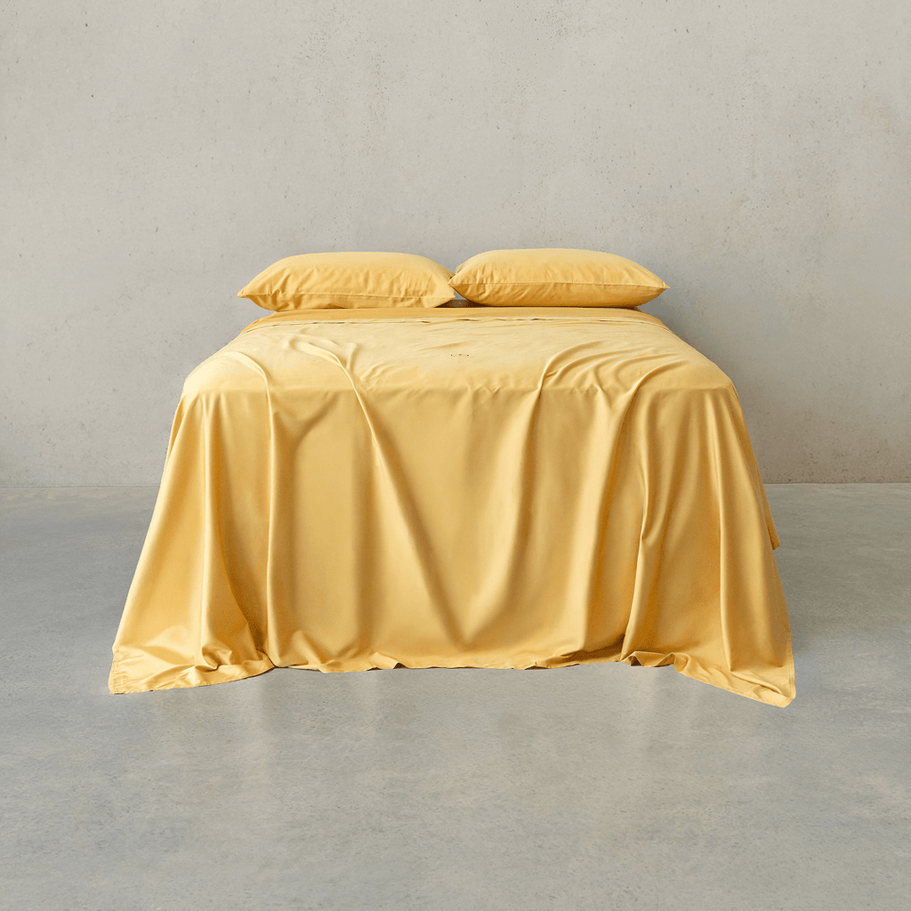 Warm golden yellow bed sheet set draped over a double bed with two matching pillowcases against a neutral wall