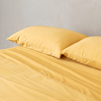Angle view of two golden yellow pillowcases and a matching flat sheet neatly arranged on a bed