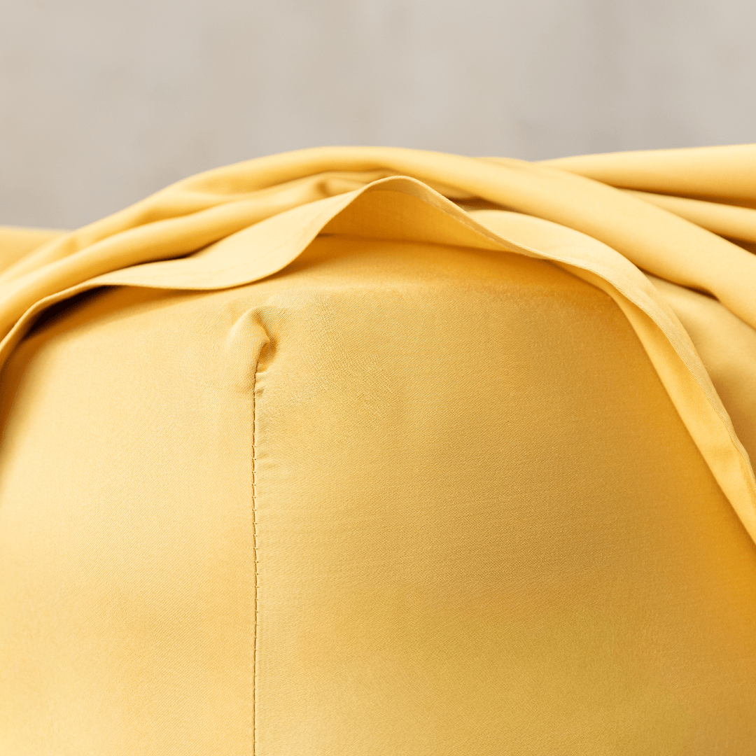 Close-up corner detail of a golden yellow fitted sheet and top flat sheet showing smooth texture and seam stitching