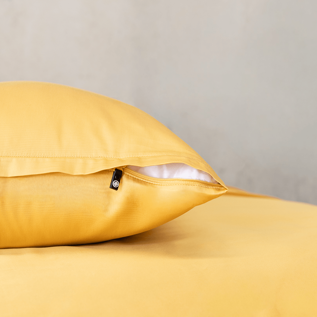 Close-up of a golden yellow pillowcase showing a partially open zipper closure revealing white pillow fill