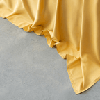 Close-up of golden yellow sheet fabric cascading smoothly onto a light gray concrete floor