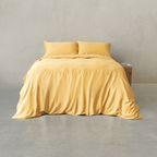 Golden yellow quilt cover set made up on a double bed with two matching pillowcases against a concrete wall