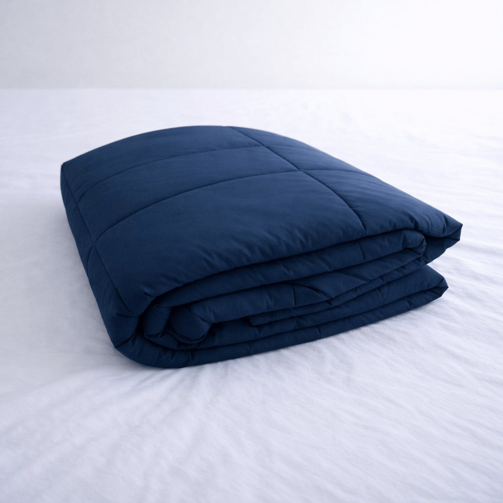 Folded navy blue cooling blanket on a white bed.