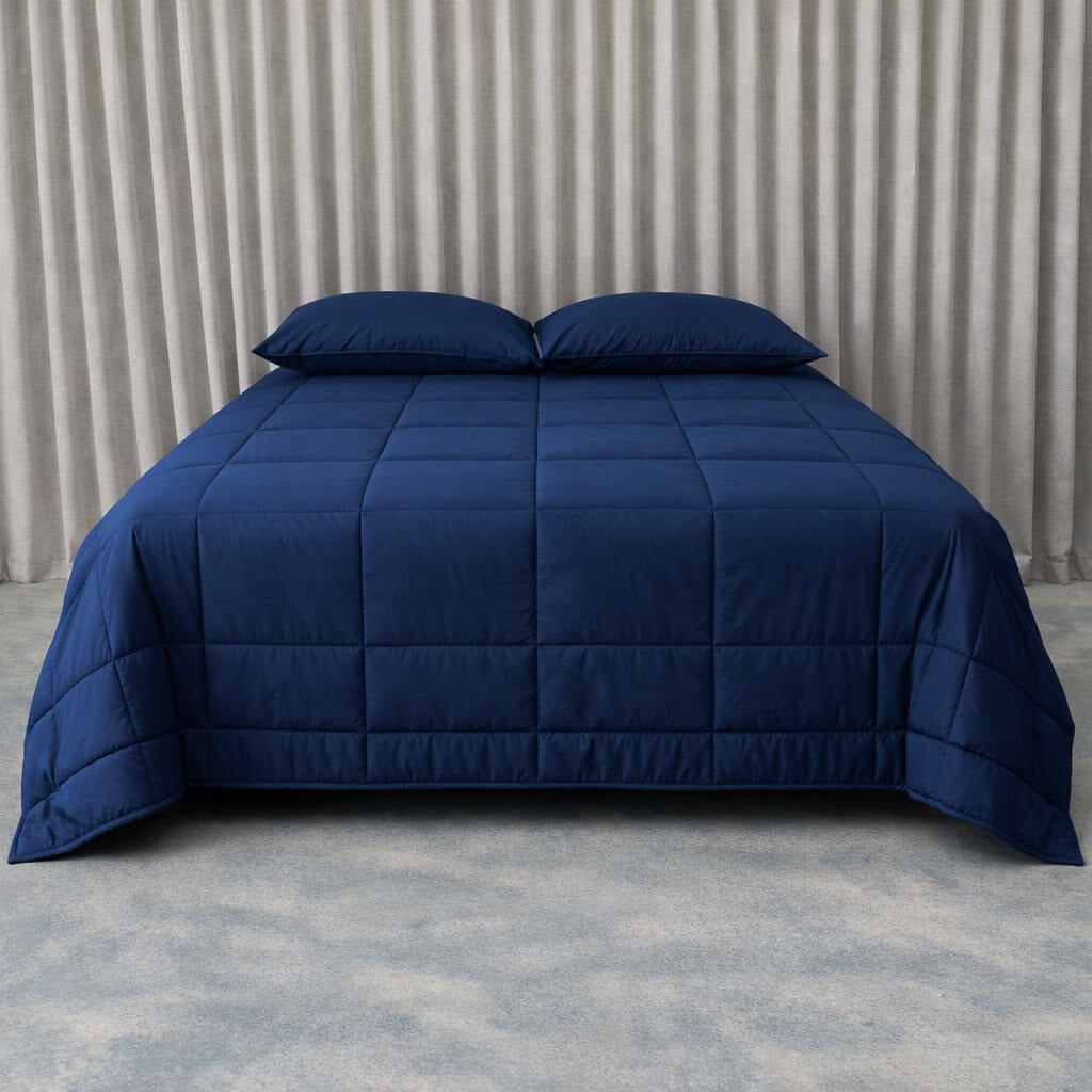 Navy blue cooling blanket on a bed with pillows against a neutral background.