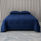 Navy blue cooling blanket on a bed with pillows against a neutral background.