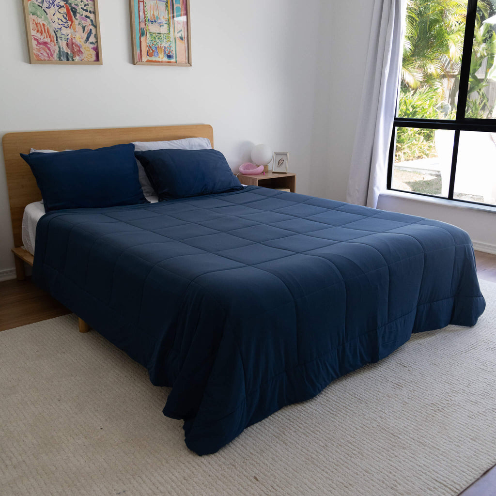 Bed with blue cooling blanket in a room with a window and wall art.