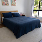Bed with blue cooling blanket in a room with a window and wall art.