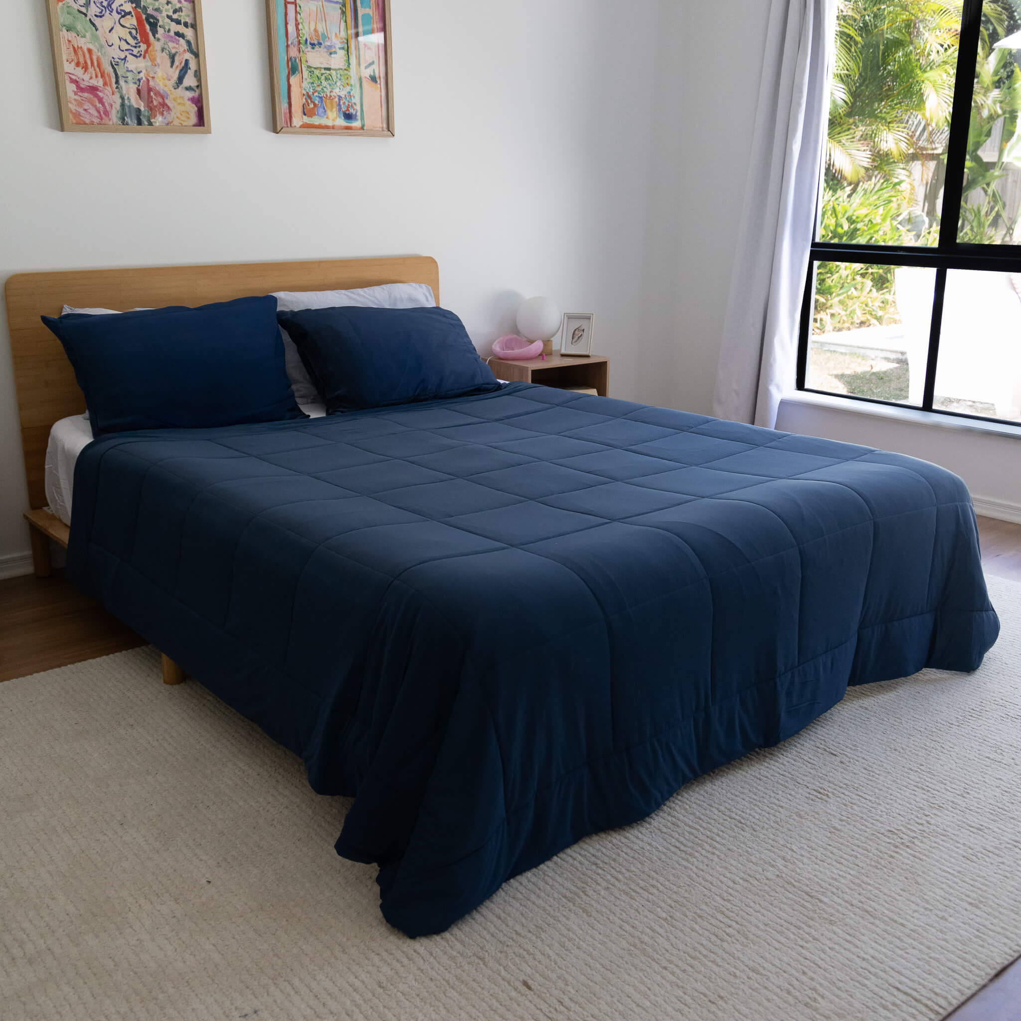 Bed with blue cooling blanket in a room with a window and wall art.