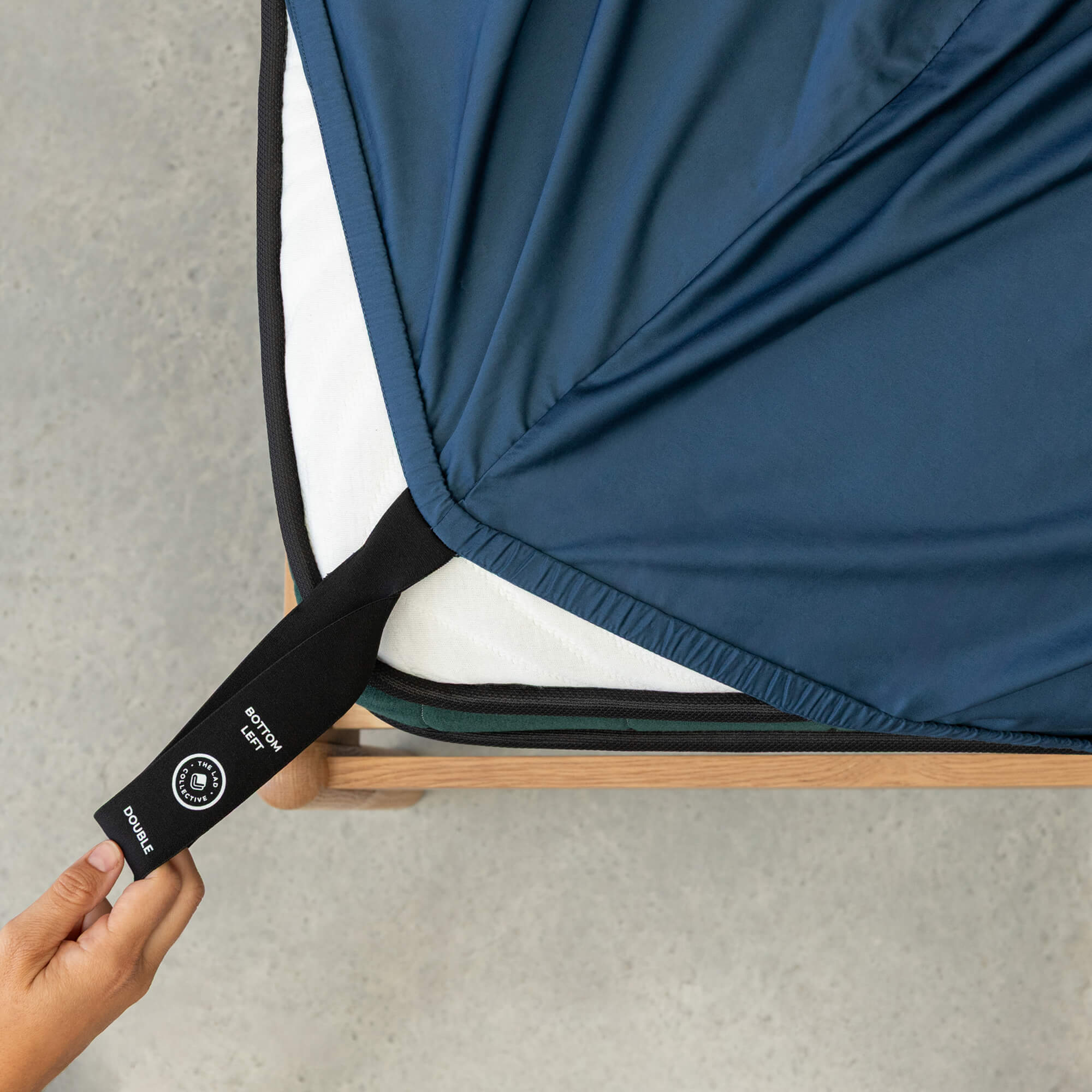 Person adjusting a blue fitted sheet with a black strap on a gray surface