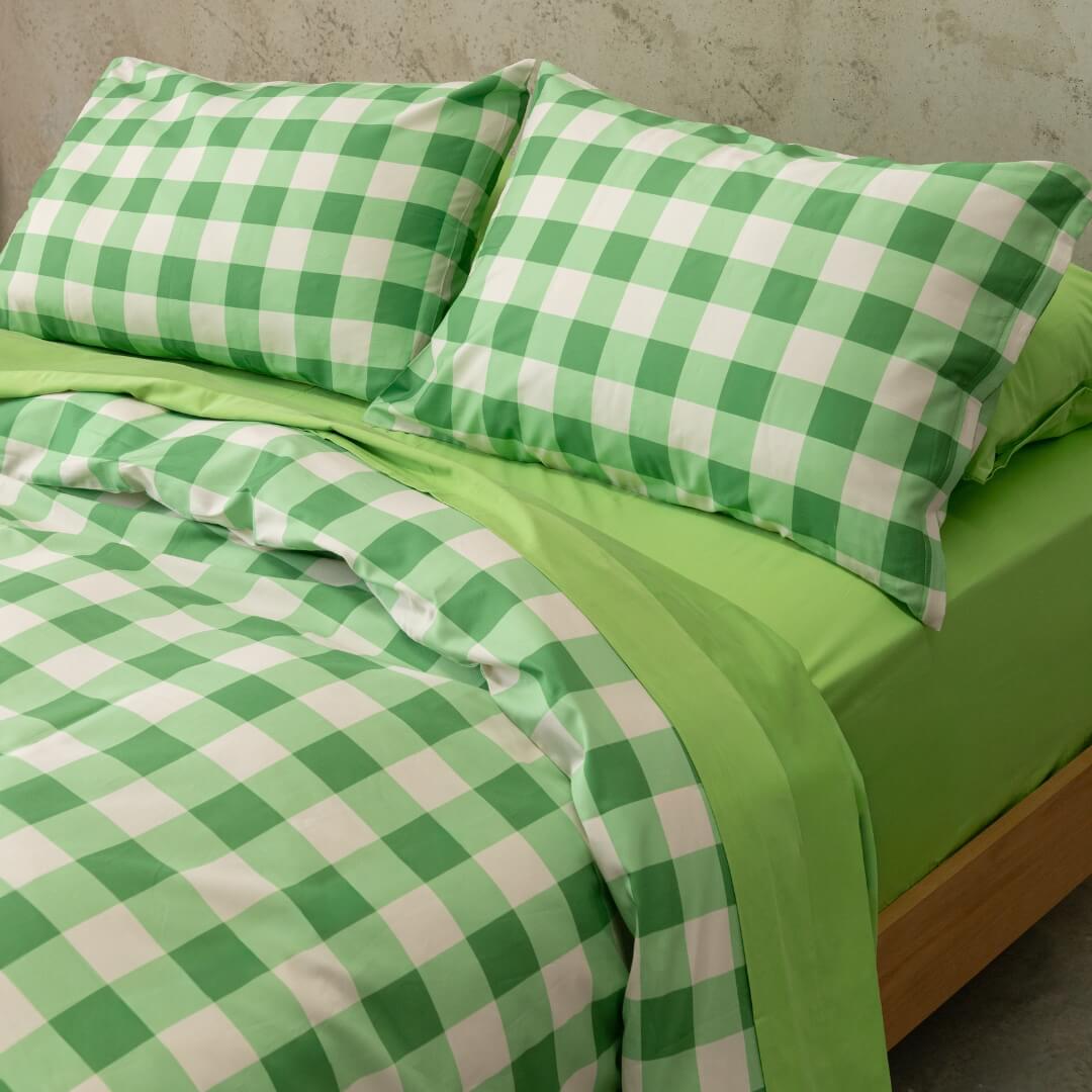 Meadow green gingham print quilt cover set on a bed, against a neutral concrete look backdrop.
