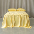 Yellow bedspread on a bed with matching pillows against a neutral background.