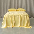 Yellow bedspread on a bed with matching pillows against a neutral background.