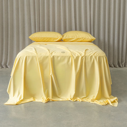 Yellow bedspread on a bed with matching pillows against a neutral background.