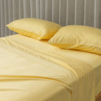 Yellow bed sheets and pillows on a bed with a gray curtain background.