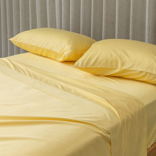 Yellow bed sheets and pillows on a bed with a gray curtain background.