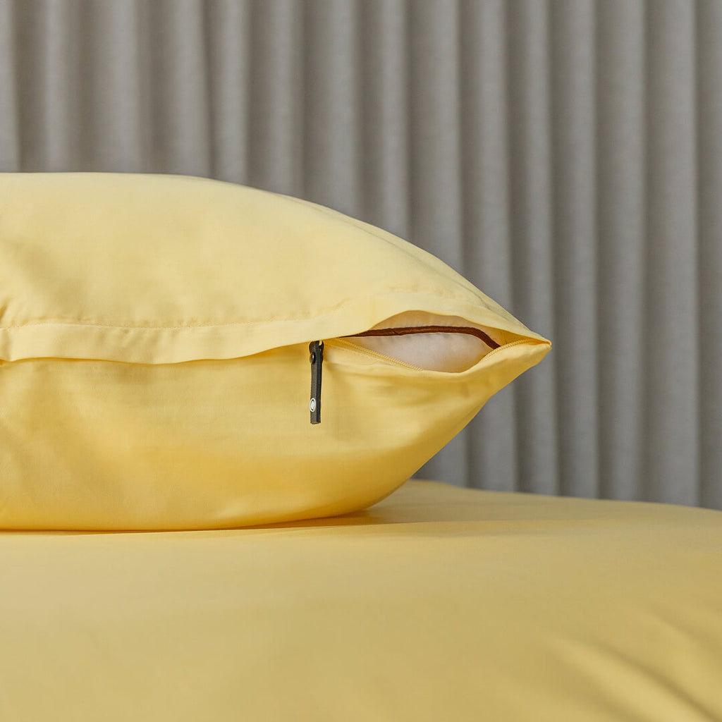 Yellow pillow on a bed with a neutral background. Featuring invisible zipper.