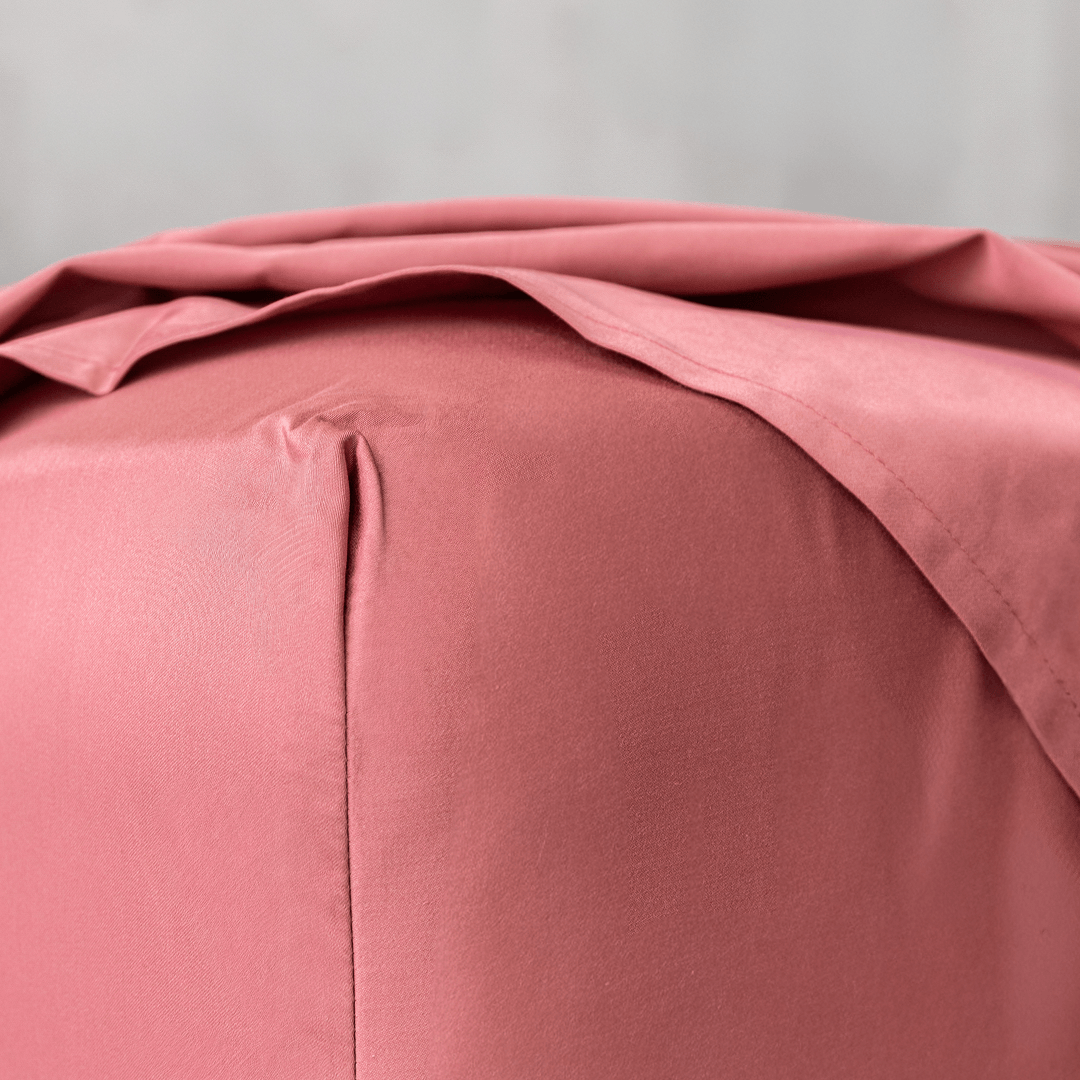 Close-up corner detail of a dusty rose pink fitted sheet and top flat sheet showing smooth fabric texture and seam stitching