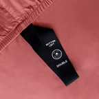 Close-up of a black corner elastic strap on a dusty rose pink fitted sheet printed with 'Bottom Left' position label