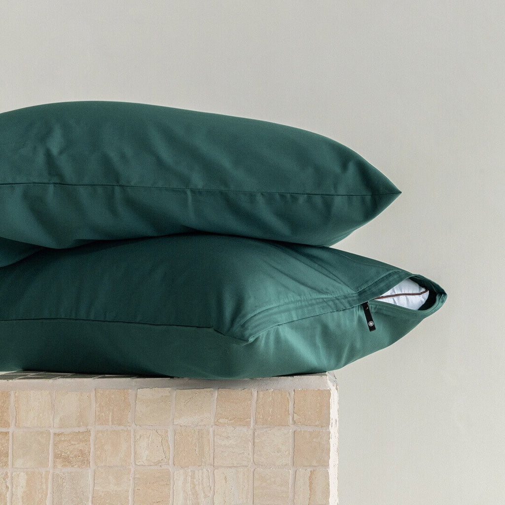 Two green pillows stacked on a beige surface with a neutral background.