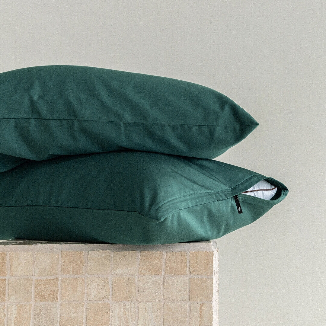 Two green pillows stacked on a beige surface with a neutral background.