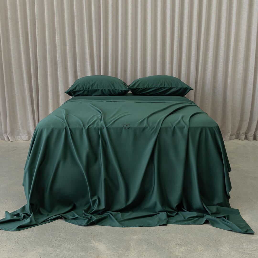Green bedspread on a bed with pillows against a beige curtain background