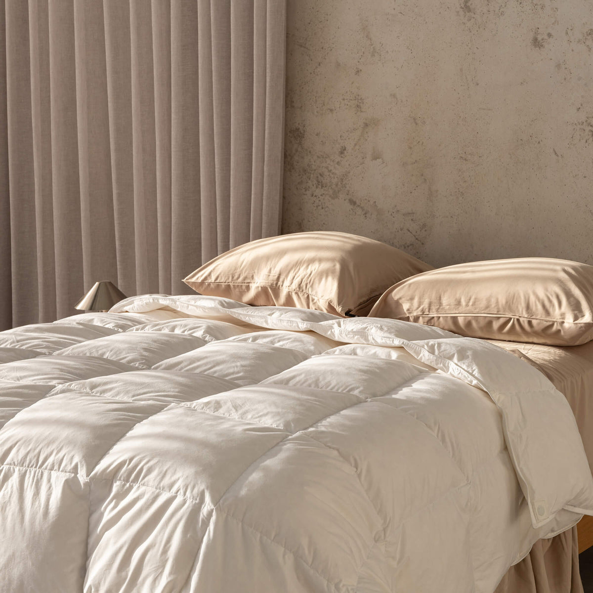 Beige quilt insert and pillows on a bed with a neutral wall and curtain in the background.