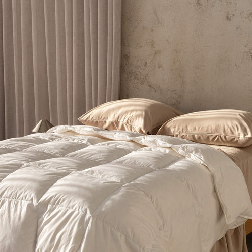 Beige quilt insert and pillows on a bed with a neutral wall and curtain in the background.