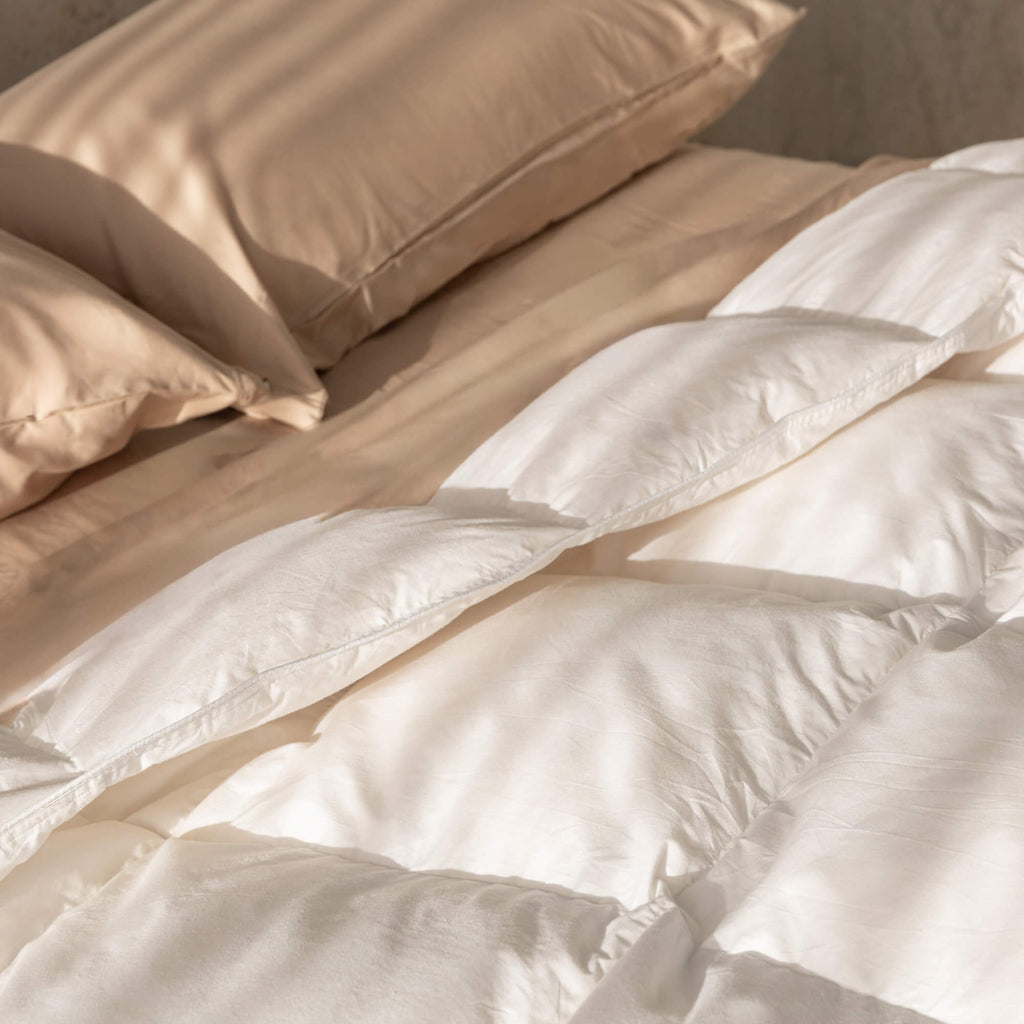 Beige comforter and pillows on a bed with a neutral background.