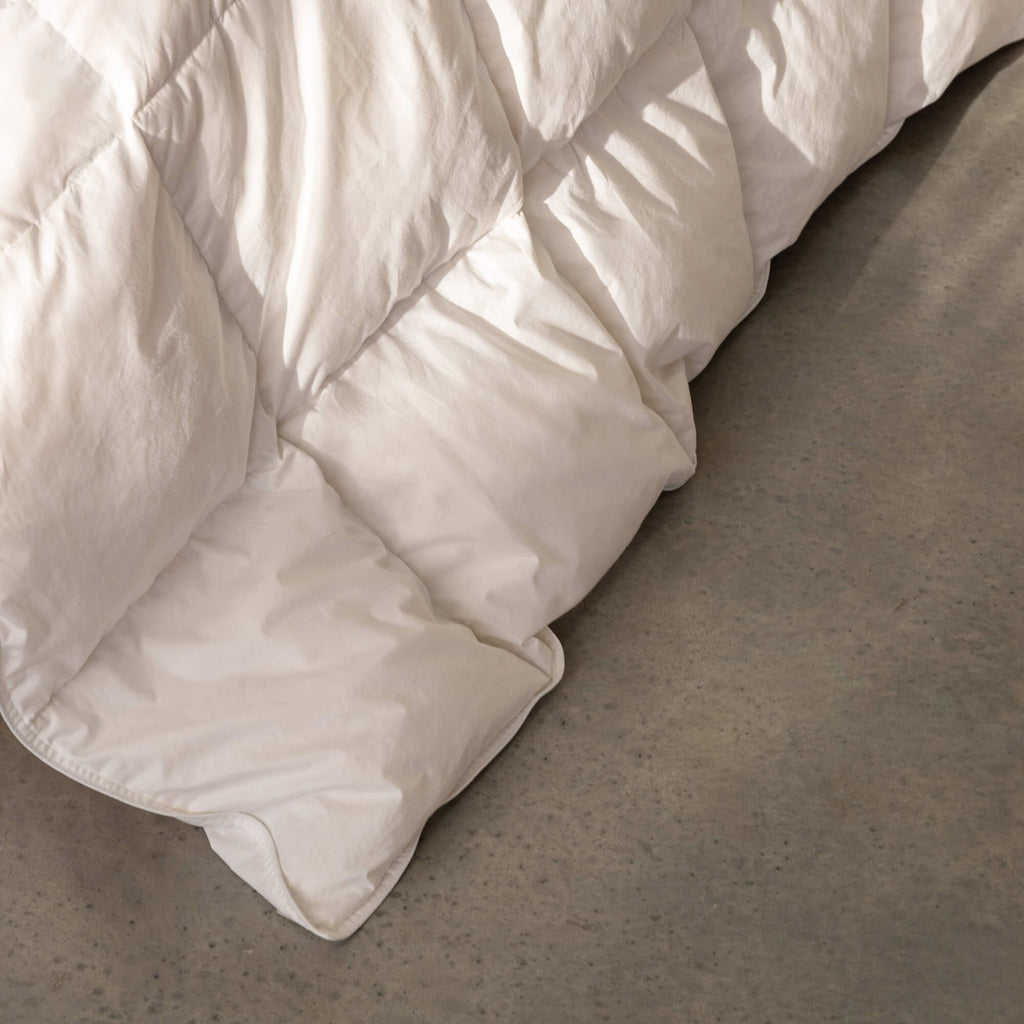 White quilted comforter on a bed with a neutral background.
