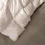 White quilted comforter on a bed with a neutral background.