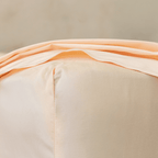 Close-up corner detail of a peach fitted sheet and top flat sheet showing smooth fabric texture and seam stitching